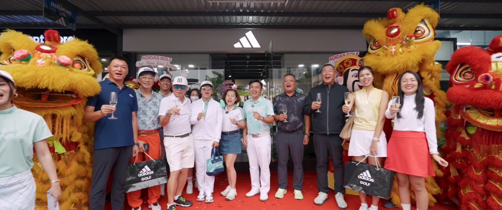 Khách mời nâng ly trước cửa hàng adidas Golf trong lễ khai trương, hai con lân vàng và đỏ đứng hai bên