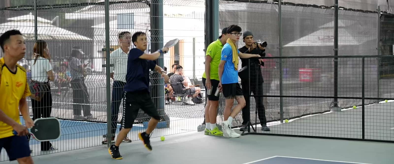 Vận động viên đánh pickleball trong sân quây lưới, quay phim ghi hình sát biên sân