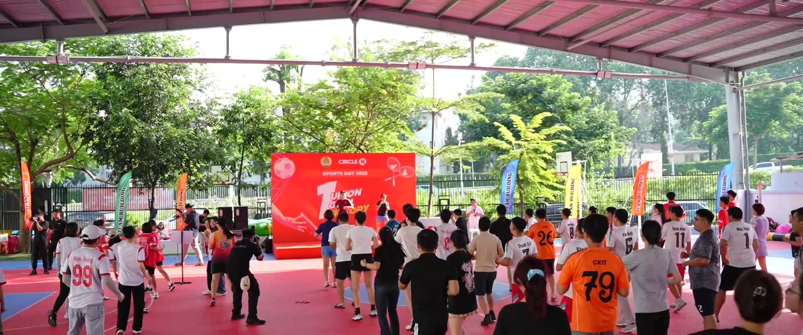 Người tham dự khởi động trước sân khấu Circle K Sport Day dưới mái che sân thể thao ngoài trời