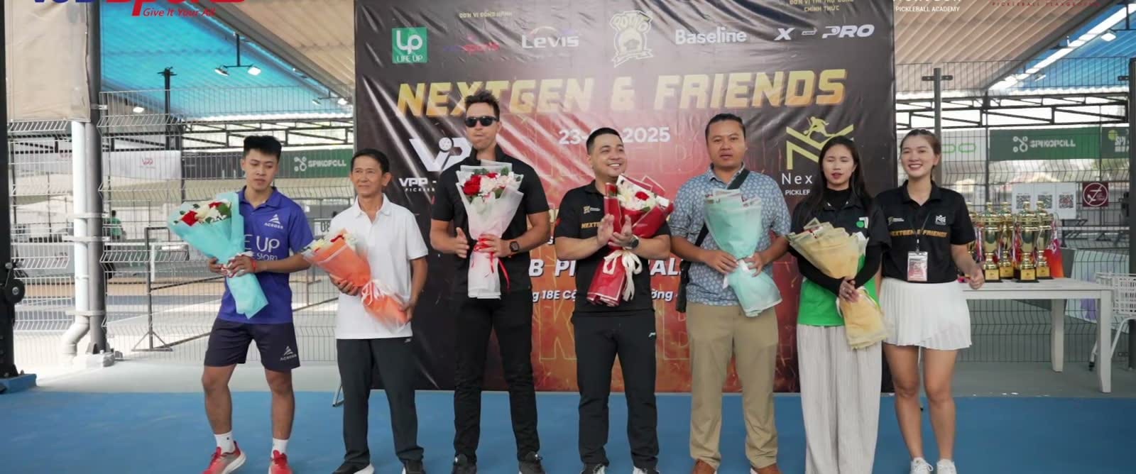 Nhóm người cầm hoa và cúp chụp ảnh trước backdrop giải pickleball NextGen and Friends