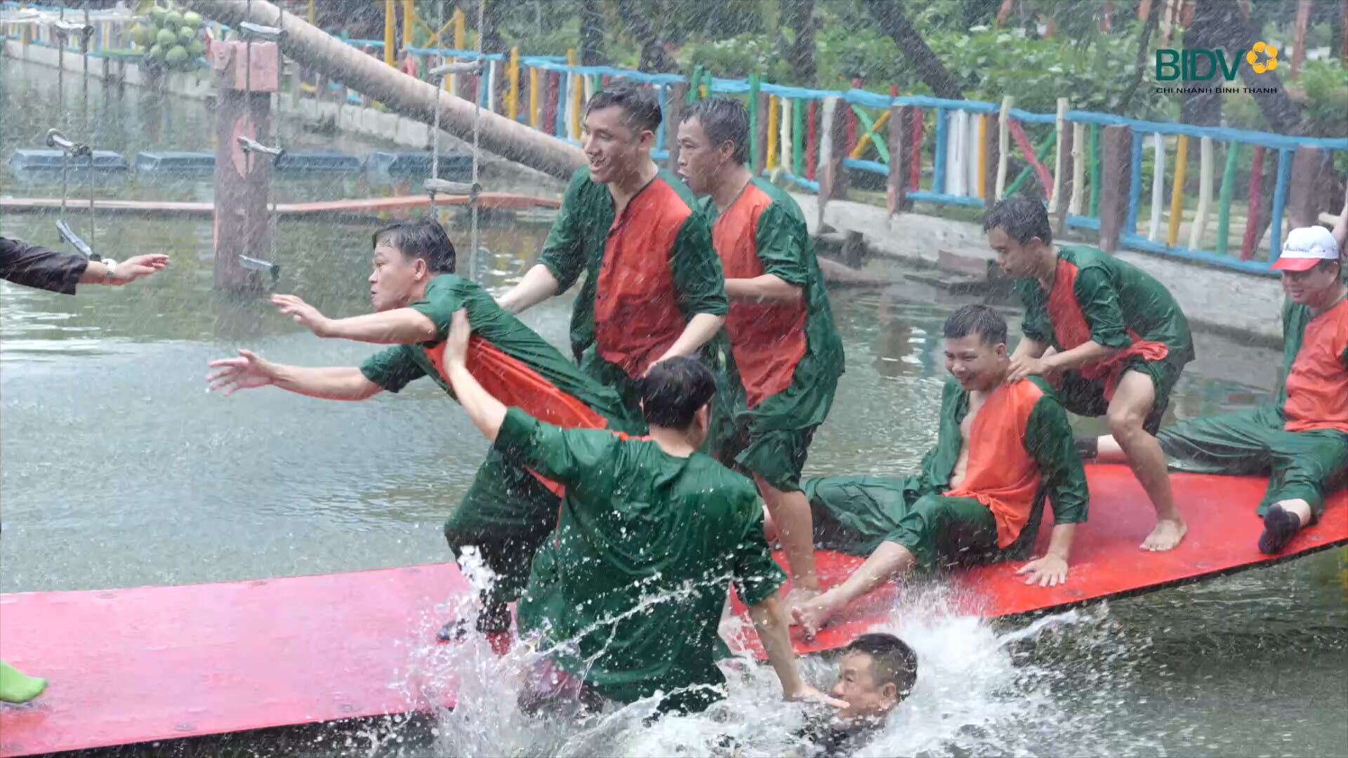 Nhóm nhân viên mặc đồ xanh ngã xuống nước khi vượt cầu trong trò chơi team building
