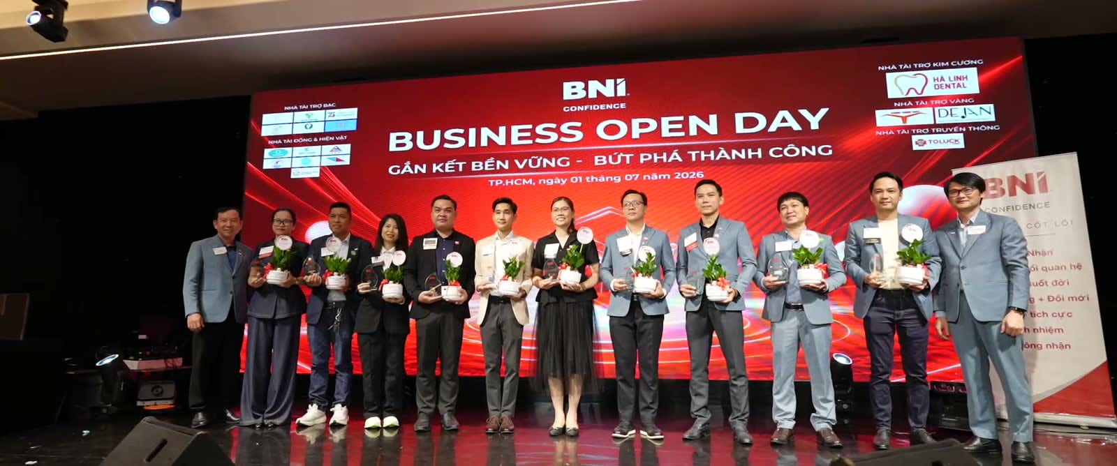 Các thành viên BNI cầm chậu cây đứng thành hàng trên sân khấu Business Open Day