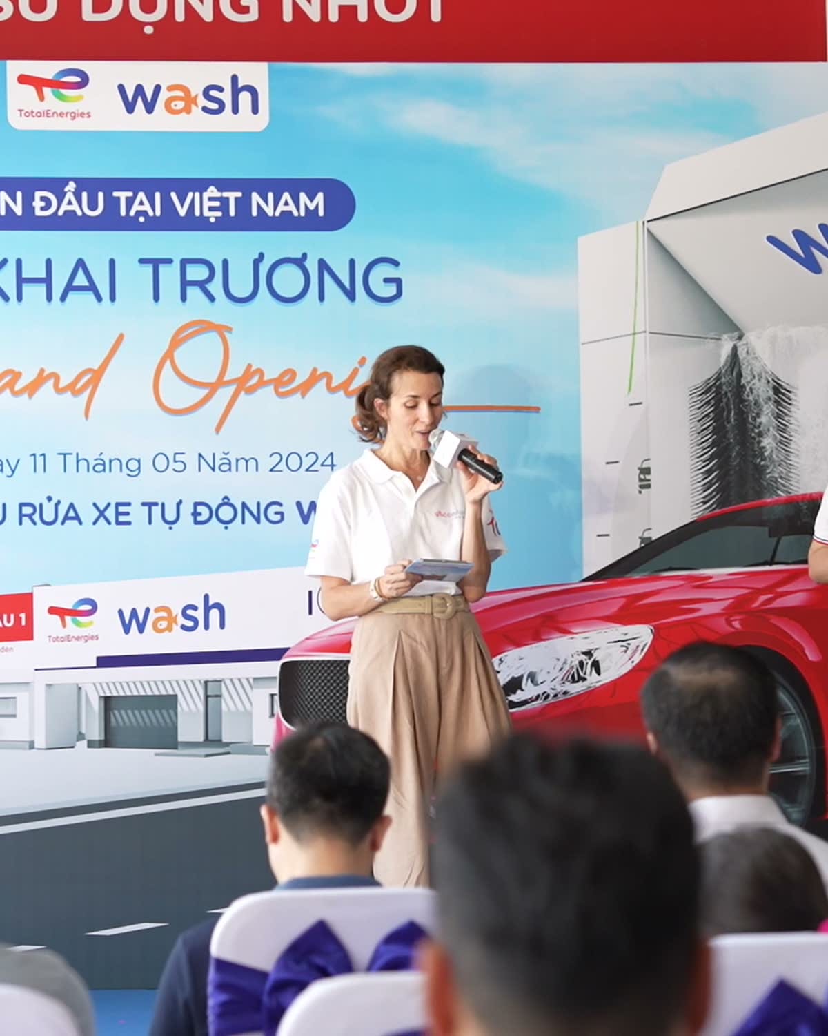 Hai người giới thiệu đứng trước màn hình Grand Opening của Wash.