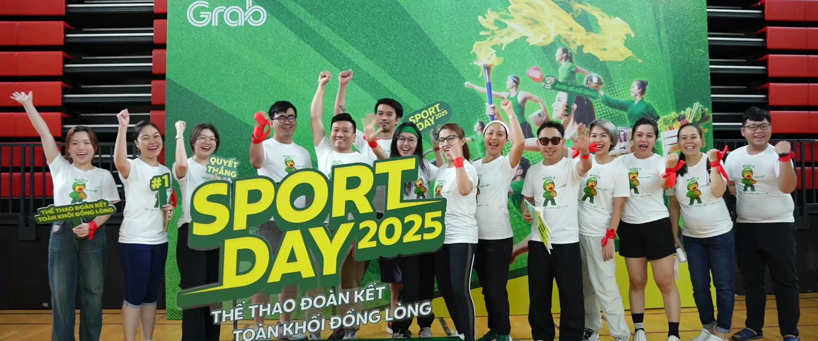 Đội ngũ Grab đứng cùng bảng Sport Day 2025 trong nhà thi đấu.